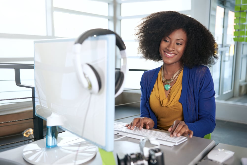 Portrait of a smiling woman with an afro at the computer in bright glass office